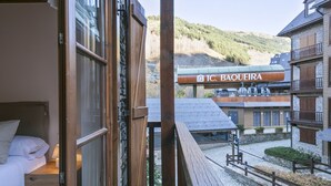 Une chambre d’hôtel avec un balcon en bois donnant sur une place pavée et offrant une vue sur la montagne.