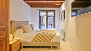 Une chambre avec un plafond en bois, un lit recouvert de draps blancs, une couverture à rayures et une fenêtre donnant sur un balcon.