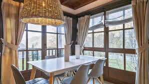 Un coin repas avec une table blanche et quatre chaises grises, de grandes fenêtres avec des rideaux et un luminaire en matière tressée.