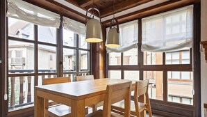 A wooden dining table with chairs, large windows, and hanging pendant lights in a room with wooden beams. - Luderna - Apartamento Val de Ruda A6 Porèra (Baqueira)