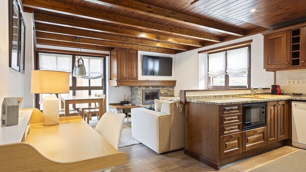 A modern kitchen with wooden beams, a stone fireplace, and a dining area with a table and chairs. - Luderna - Apartamento Val de Ruda A6 Porèra (Baqueira)