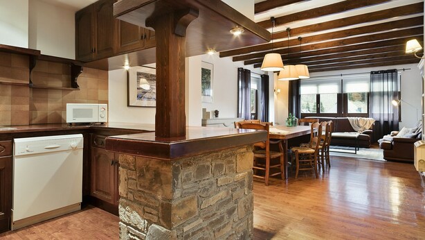 A spacious kitchen with a stone island, wooden beams, and a dining area with a sofa and chairs. - Luderna - Apartamento con terraza Bonaigua B2 (Baqueira)