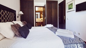 A hotel room with a large bed, two wardrobes, a bathroom visible through an open door, and a flat-screen TV mounted on the wall. - Luderna - Apartamento con terraza Bonaigua B2 (Baqueira)