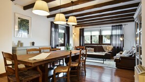 A dining area with a wooden table and chairs, a sofa, and a large window with curtains. - Luderna - Apartamento con terraza Bonaigua B2 (Baqueira)