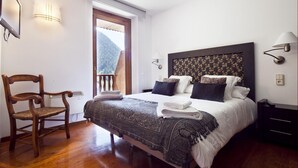 A bedroom with a large bed, a wooden chair, a nightstand, and a window with a view of a forest. - Luderna - Apartamento con terraza Bonaigua B2 (Baqueira)