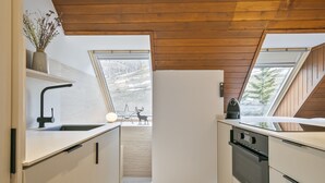 A modern kitchen with white cabinetry, a black faucet, and a stove. There are skylights allowing natural light and a view of the outdoors.
