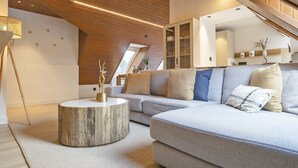 A modern living room with a wooden ceiling, a round coffee table, a grey sofa, and a staircase leading to an upper level.