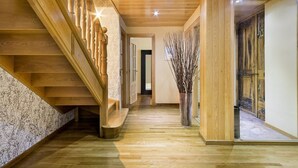 Un escalier en bois, avec un mur de marbre sur le côté gauche, mène à un couloir où se trouve un vase rempli de branches.