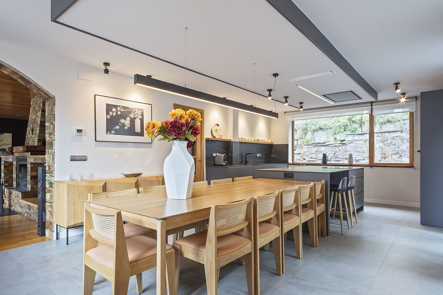 Une cuisine moderne dotée d’un îlot central, d’un coin repas avec des meubles en bois et d’une grande fenêtre offrant une vue sur l’extérieur.