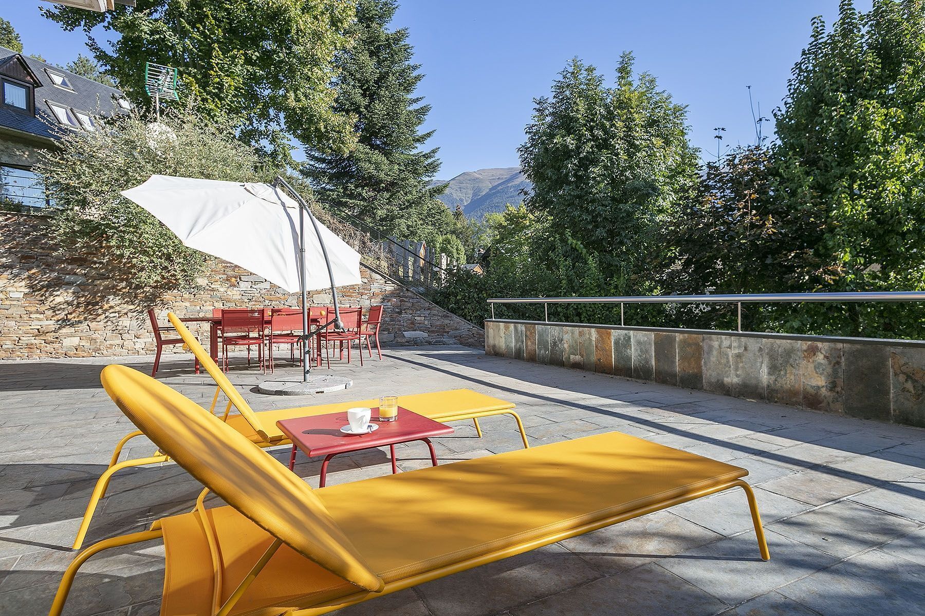 An outdoor seating area with yellow chairs and a table, a white umbrella, and a stone wall.