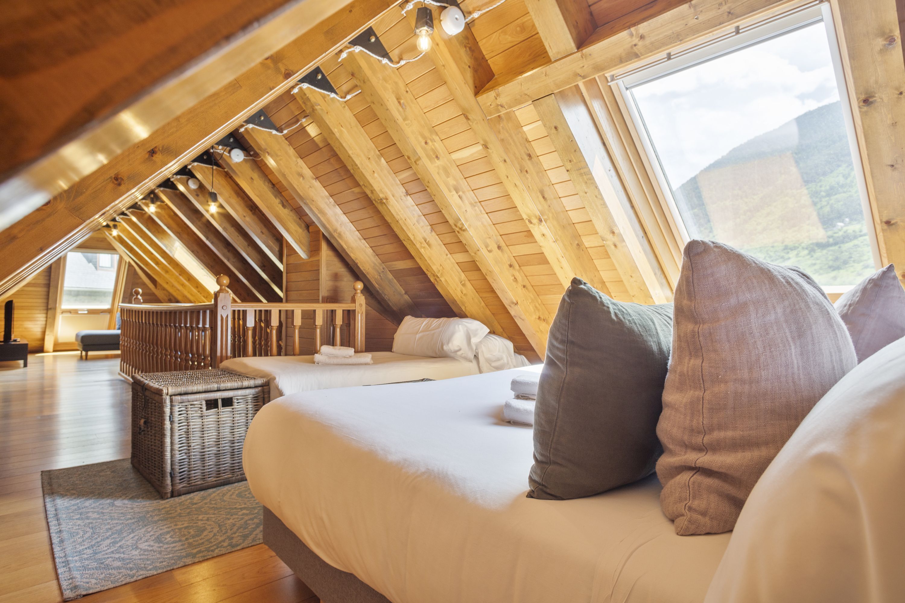 Un dormitorio acogedor en el ático, con techo inclinado, un ventanal grande y una cama con almohadas.