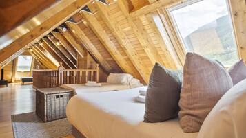 Un dormitorio acogedor en el ático, con techo inclinado, un ventanal grande y una cama con almohadas.