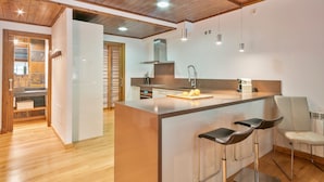 Een moderne keuken met een centraal eiland, barkrukken en een houten plafond.