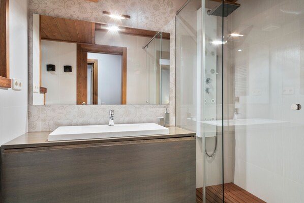 A modern bathroom with a glass-enclosed shower, a large mirror, and a wooden vanity. - Luderna - Casa Val de Ruda II (Baqueira)