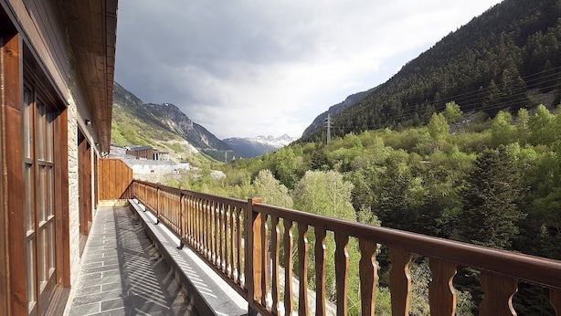 Een balkon met houten hekwerk met uitzicht op een bergachtig landschap.
