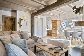 A spacious living room with a high ceiling, wooden beams, a sofa set, a coffee table, and a dining area with chairs.