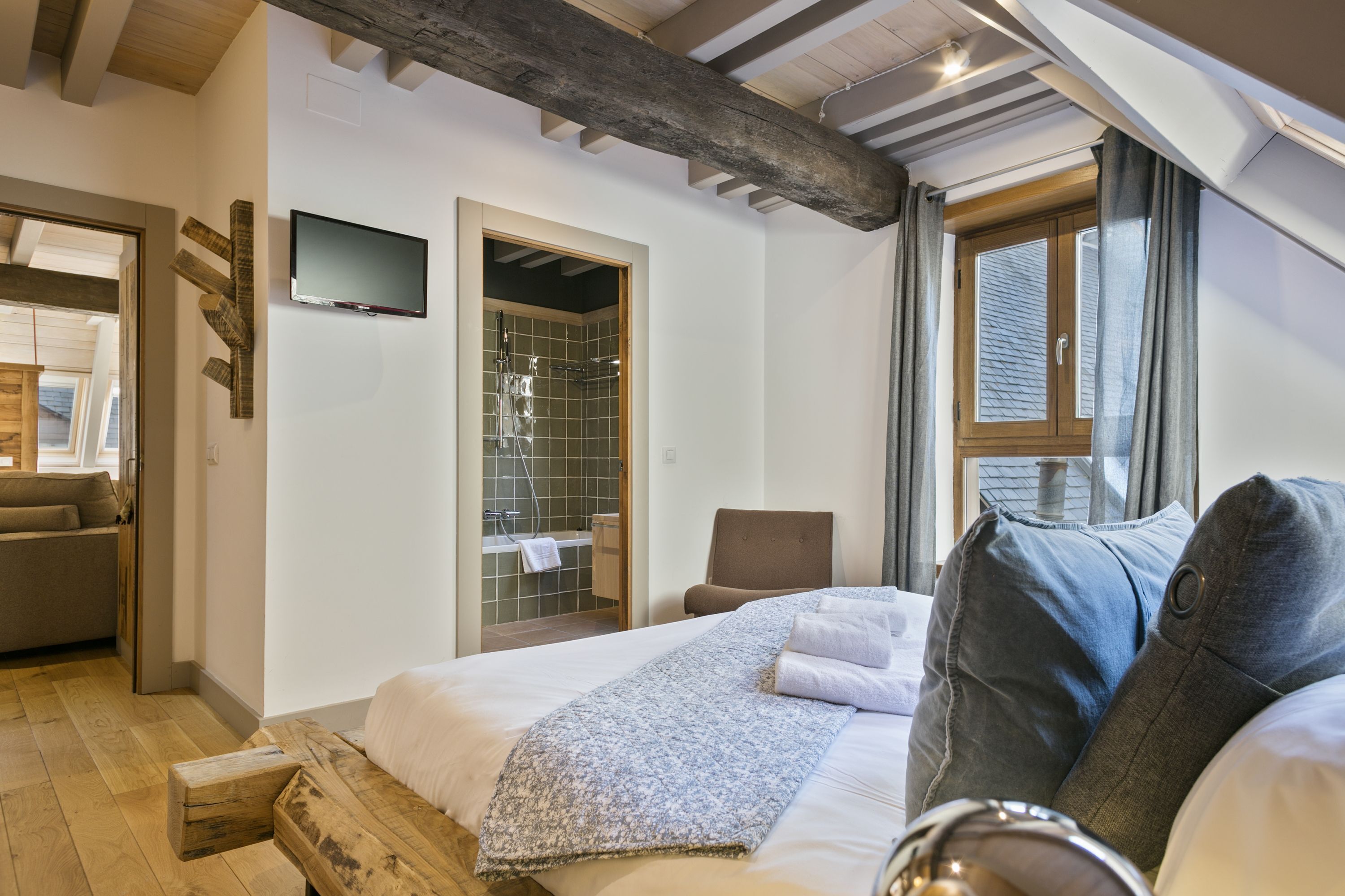 A bedroom with a bed, a chair, a TV, and a bathroom with a shower.