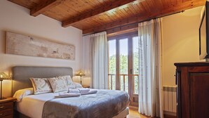 Un dormitorio con una cama grande, vigas de techo de madera, vistas a la vegetación exterior y un radiador en la pared.