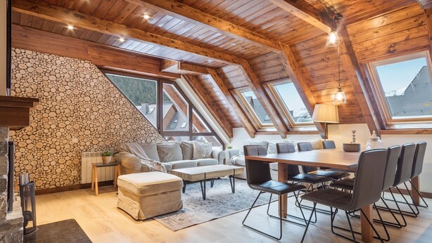 Ein geräumiger Lofts mit Steinwand, Holzbalken, einem Essbereich mit Stühlen und einem großen Fenster.