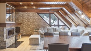 Ein gemütliches Dachzimmer mit Steinwand, Kamin, einer Couch und einem Esstisch.