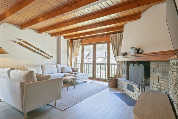 A cozy living room with a stone fireplace, wooden beams, and a sofa. - Luderna - Apartamento Dera Pincèla (Vielha)
