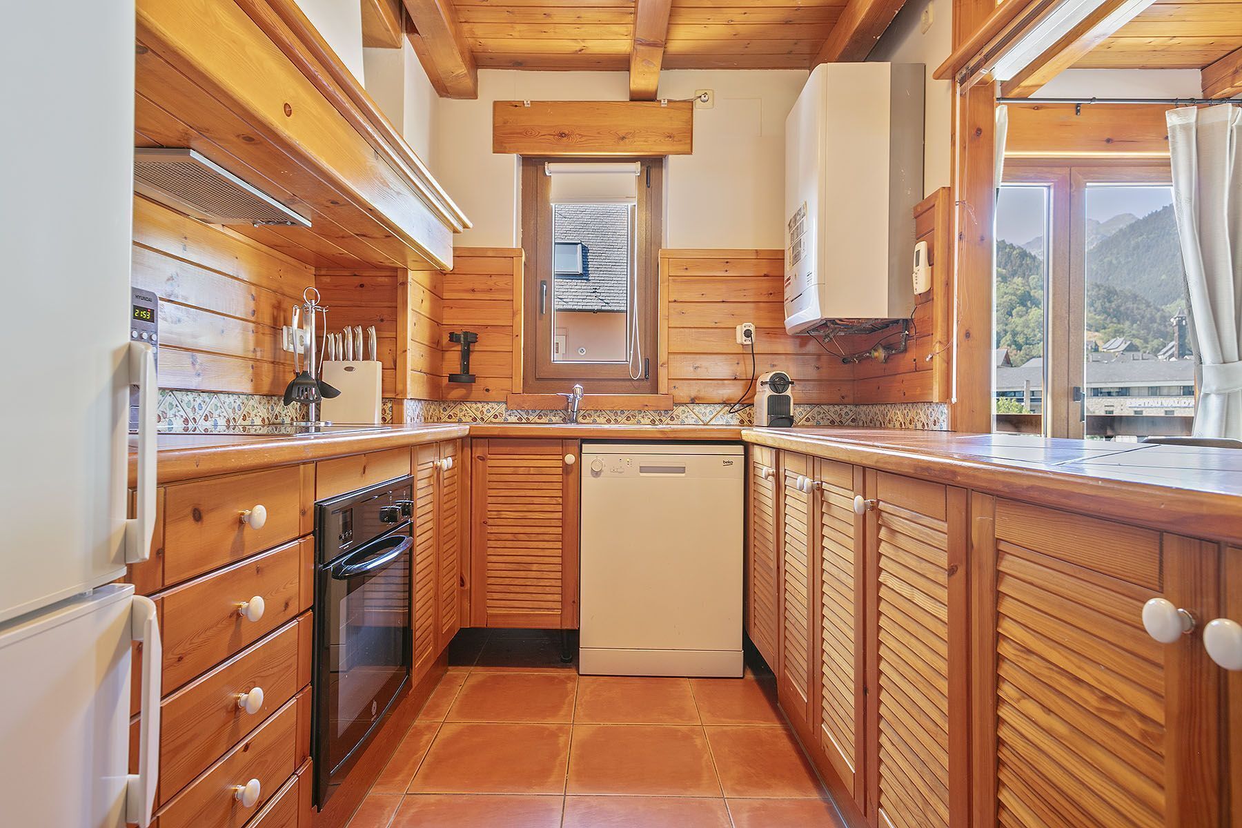 Une cuisine avec des meubles en bois, un lave-vaisselle et une fenêtre donnant sur les montagnes.