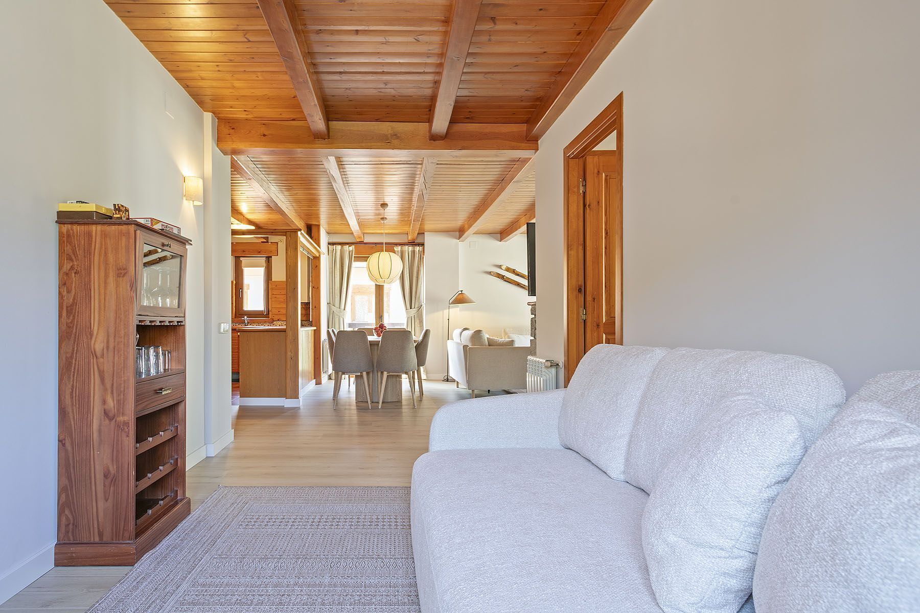 Un vaste espace de vie doté d’un plafond en bois, d’un canapé, d’une table à manger avec des chaises, et d’un coin cuisine à l’arrière-plan.
