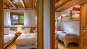 Una camera accogliente con due letti singoli, una cuccetta a castello, pavimento in legno, una finestra con tende e un comodino con una lampada.