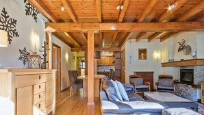 Un accogliente interno di una baita con soffitto in legno, un camino e un divano con cuscini.
