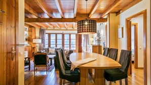 Un'area pranzo in legno con un tavolo grande e sedie, un lampadario e vista all'esterno attraverso ampie finestre.