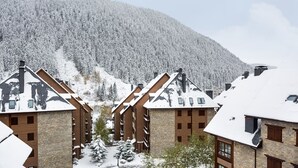 A cluster of wooden buildings with sloped roofs, surrounded by snow-covered trees and a mountain in the background. - Luderna - Apartamento Val de Ruda B2 Pradets (Baqueira)