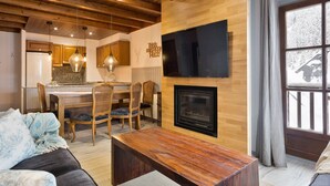 A cozy living room with a fireplace, wooden ceiling, and a dining area with a table and chairs. - Luderna - Apartamento Val de Ruda B2 Pradets (Baqueira)