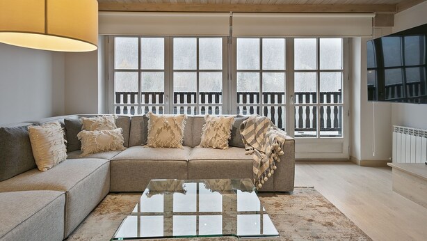 A modern living room with a sectional sofa, a glass coffee table, and large windows with a view of a balcony. - Luderna - Casa Val de Ruda IV des Artiguetes (Baqueira)