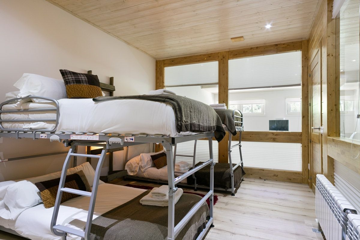 A bunk room with three bunk beds, a wooden ceiling, and a large window.