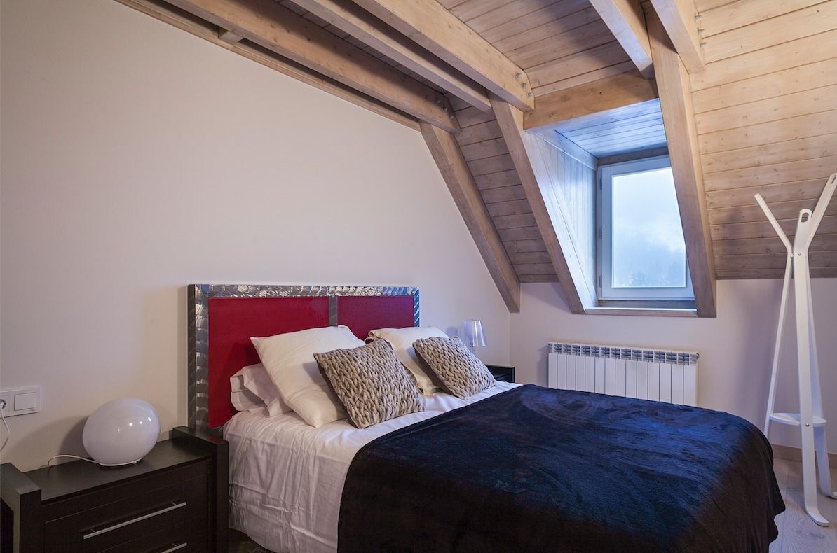 Ein Schlafzimmer mit geneigter Decke, einem Oberlicht, einem Bett mit roter Kopfteil und einem weißen Heizkörper.