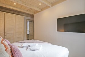 A bedroom with a bed, white linens, a wooden ceiling, and a large window.