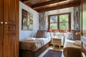 Ein gemütliches Schlafzimmer mit zwei Einzelbetten, einer Holzzielung, einem Fenster mit Blick auf Grünflächen und einem Bild an der Wand.