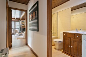 Ein modernes Badezimmer mit einem Holzbadezimmer-Möbelstück, einer Dusche und einer Toilette. Ein Flur führt zu einem Wohnbereich mit einer Couch und einem Sessel.