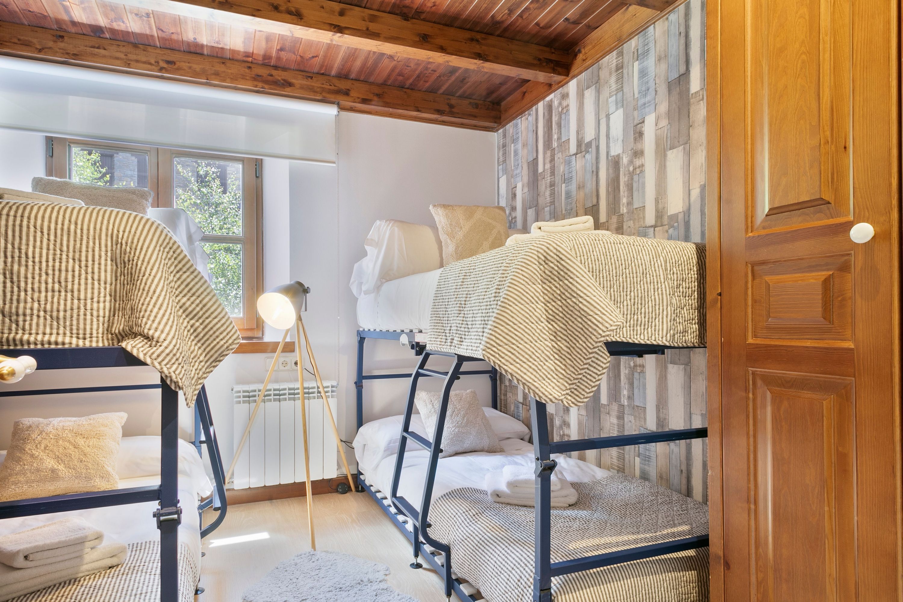 Een slaapkamer met een stapelbed, houten plafond en uitzicht op de natuur door een raam.