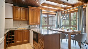 A kitchen with wooden cabinets, a granite countertop, and a dining area with a table and chairs. - Luderna - Apartamento Val de Ruda B21 Blanhiblar (Baqueira)