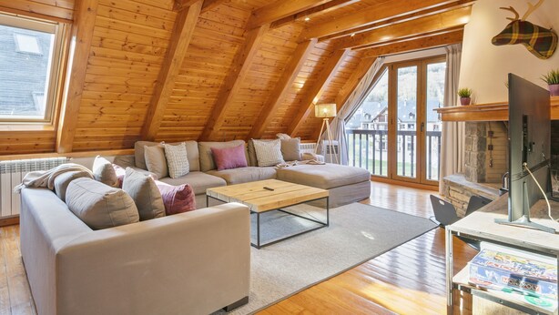 Ein gemütliches Dachzimmer mit Holzbalken, einem Sofa, einem Couchtisch und einem Kamin.