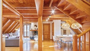 Ein geräumiger Lofts mit Holzbalken, einem Essbereich mit weißen Stühlen und einer gemütlichen Sitzecke mit einer Couch.