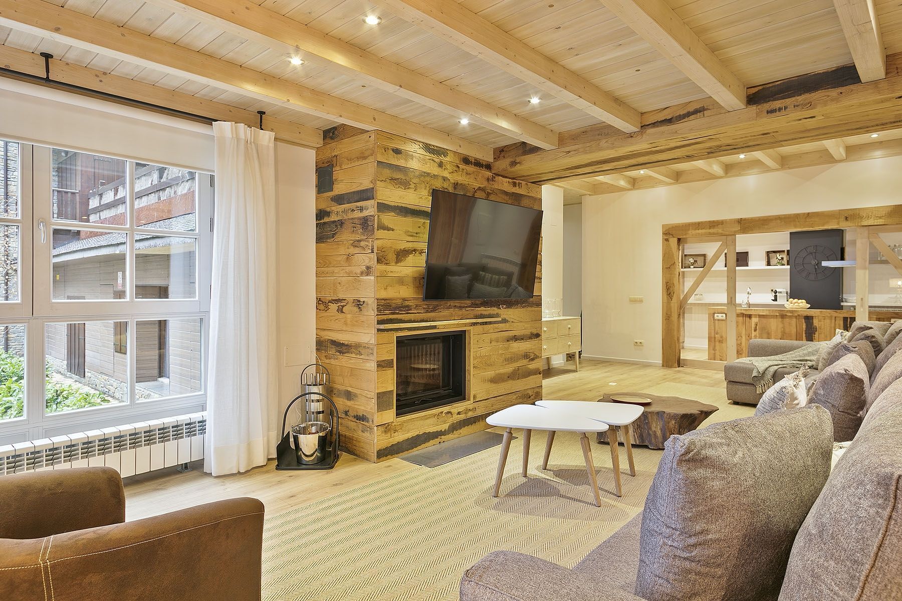 Ein gemütliches Wohnzimmer mit Kamin aus Stein, einem großen Fernseher und einer komfortablen Sitzecke mit Sofa und Sesseln.