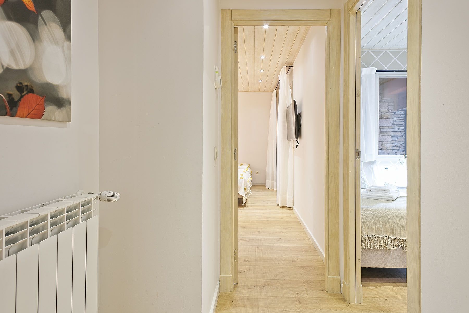 A narrow hallway with a wooden floor leading to a bedroom with a bed and a stone wall.