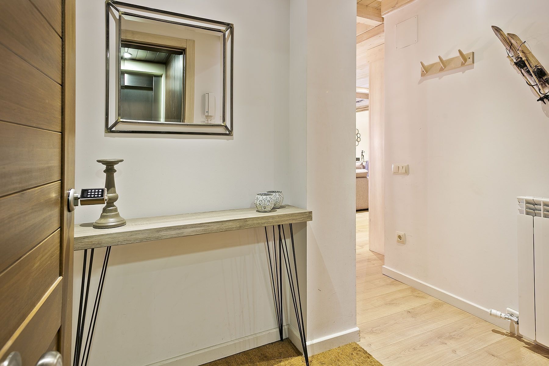 Un couloir avec une porte blanche, une petite table sur laquelle se trouvent une bougie et un bol, et un miroir accroché au mur.