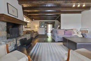 A cozy living room with a stone fireplace, wooden ceiling beams, and a comfortable seating area with sofas and a rug.