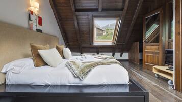 Un dormitorio con techo de madera, un tragaluz, una cama con ropa de cama blanca y un televisor sobre un mueble de madera.