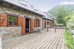 A rustic stone building with wooden shutters, a wooden deck, and a mountain backdrop. - Luderna - Casa con terraza Unhola (Bagergue)