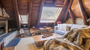 A cozy attic room with a stone fireplace, wooden beams, a sofa, and a fur throw. - Luderna - Casa Coto Moreu (Betren)