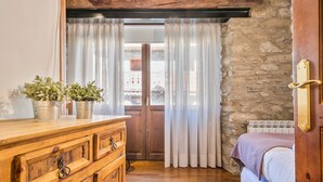 A room with a wooden dresser, a bed with a white blanket, a stone wall, and a window with sheer curtains. - Luderna - Casa Coto Moreu (Betren)